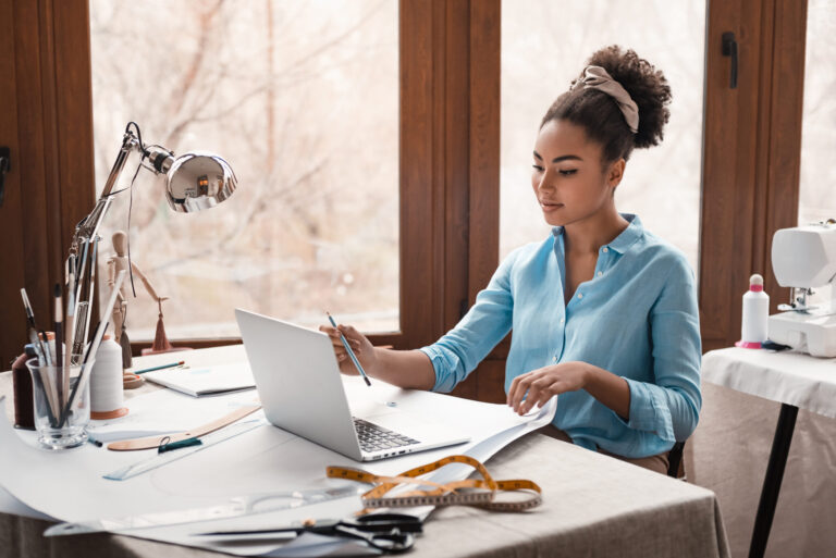 Stylist working on laptop and design sketches for business management and marketing advice