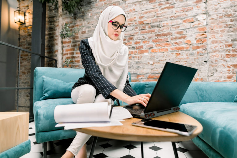 a person in a white robe sitting at a table with a laptop