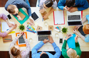 a group of people sitting around a table with laptops and papers on it