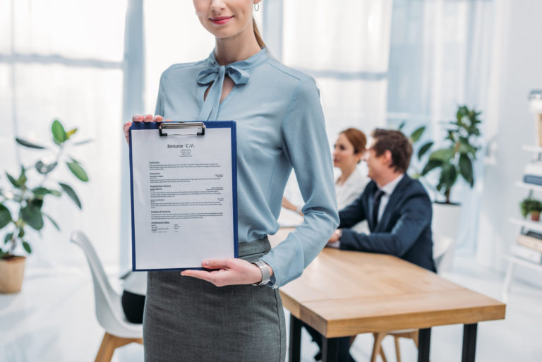 cropped view of cheerful recruiter holding clipboard with resume cv lettering near coworkers